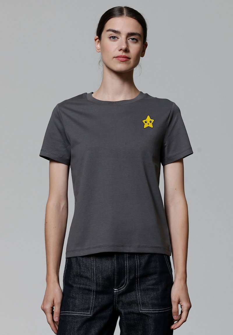 Graues Baumwoll-T-Shirt mit kurzen Ärmeln, das mit einem gelben sternförmigen gestickten Aufnäher auf der linken Brust versehen ist. Schlichter, lockerer Schnitt.