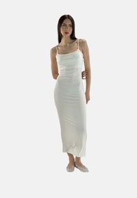 Abito maxi bianco aderente realizzato in tessuto morbido, con sottili spalline e silhouette dritta, abbinato a scarpe flat argentate.