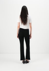 Black flared jeans with a waistband, two back pockets, and subtle stitching details, paired with a white t-shirt and black heels.