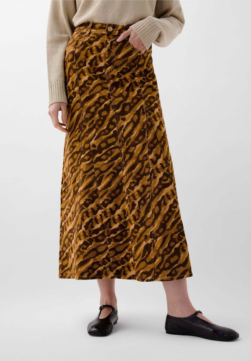 Jupe maxi en velours côtelé marron à motifs avec des coutures verticales et une fermeture à bouton, portée avec des chaussures plates noires. Le tissu a une finition texturée.