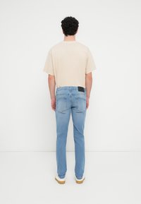 Μπεζ κοντομάνικο T-shirt σε συνδυασμό με ανοιχτό μπλε τζιν παντελόνι με ίσια γραμμή, πίσω τσέπες και μαύρο δερμάτινο έμπλαστρο στη μέση.