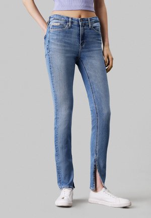 Jean en denim bleu clair avec une coupe slim, dotés d'une fermeture à bouton à l'avant, de décolorations et d'un ourlet fendu au niveau de la cheville.