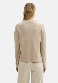 Beige gestrickter Pullover mit Rundhalsausschnitt, langen Ärmeln und einem leicht gekürzten Saum, der eine strukturierte Oberfläche aufweist.