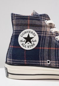 High-Top Converse Sneakers aus kariertem Stoff in Marineblau, Beige und Rot. Mit einem weißen Logo-Patch und einer schwarzen Gummisohle.