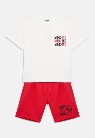 Λευκό κοντομάνικο T-shirt με το λογότυπο Moschino στην τσέπη, σε συνδυασμό με κόκκινα σορτς που φέρουν το ίδιο λογότυπο στο αριστερό πόδι.