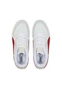 Un paio di sneakers bianche Puma con lati in suede rosso, lacci bianchi, punte perforate e solette con marchio viste dall'alto su sfondo bianco.