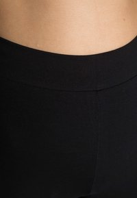 Leggings pretas sem costura com uma textura suave e elástica. A cintura é larga e macia, proporcionando conforto sem fechos visíveis.