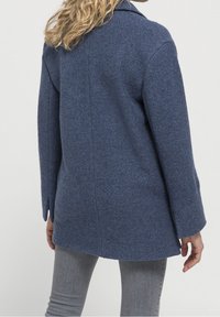 Blå ullblandad kappa med en avslappnad passform, slagkrage, långa ärmar och sidoflikar. Slät textur, längd till mitten av låret och minimala sömmar.