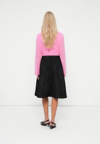 Långärmad rosa topp med rund halsringning, parat med en knälång svart strukturerad kjol, med blommönster och åtsittande midjeband.