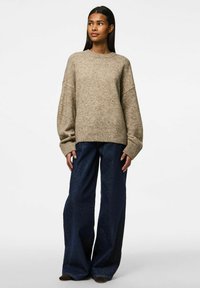 Beige stickad tröja med ribbad nederkant, vida ärmar, bärs tillsammans med mörka denim byxor med vida ben. Strukturerat mönster över hela tröjan.