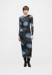 Fekete hosszú ujjú ruha kék virágmintával, könnyű hálós anyagból, testhezálló sziluettel és oldalsó ráncolással, térd magas fekete csizmával párosítva.