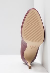Chaussure à talon haut bordeaux avec une tige en cuir lisse et un bout effilé. La semelle extérieure est en caoutchouc beige avec des rainures horizontales pour une meilleure adhérence.