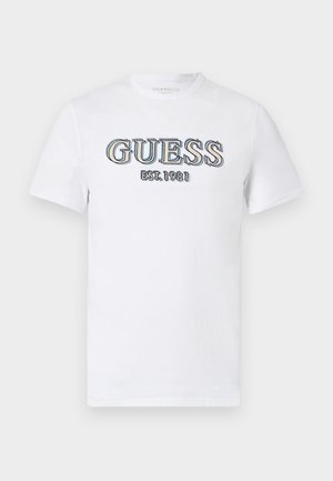 Balta trumpomis rankovėmis marškinėliai, pagaminti iš medvilnės, su spalvotu siuvinėtų "GUESS" logotipu ir "EST. 1981" tekstu priekyje.