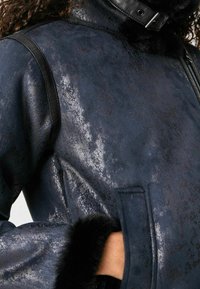 Czarna, sztuczna skórzana kurtka o ciemnoniebieskim kolorze z fakturowanym wykończeniem, czarnym futrzanym kołnierzem i kieszeniami. Posiada gładkie czarne akcenty oraz zamek błyskawiczny.