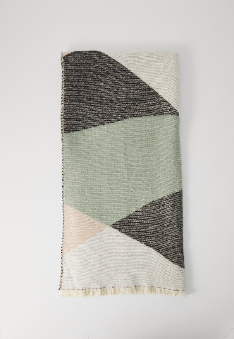 Foldet vævet tekstil med geometriske former i sort, grøn, beige og hvid på en lys baggrund.