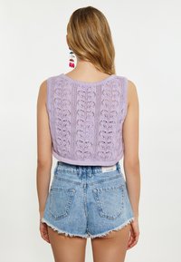 Lila neulottu crop-top, jossa on lehväkuvio, yhdistettynä korkeavyötäröisiin vaaleansinsisiin farkkushortseihin, joissa on hapsureunat ja takataskut.