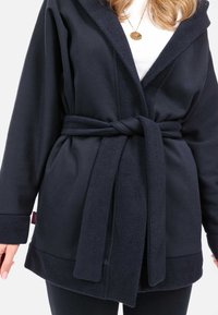Navy-Fleece-Umhang mit Kapuze, ausgestattet mit einem Gürtel, seitlichen Taschen und einem strukturierten Kragen. Weicher, glatter Stoff mit kontrastierenden Kanten.