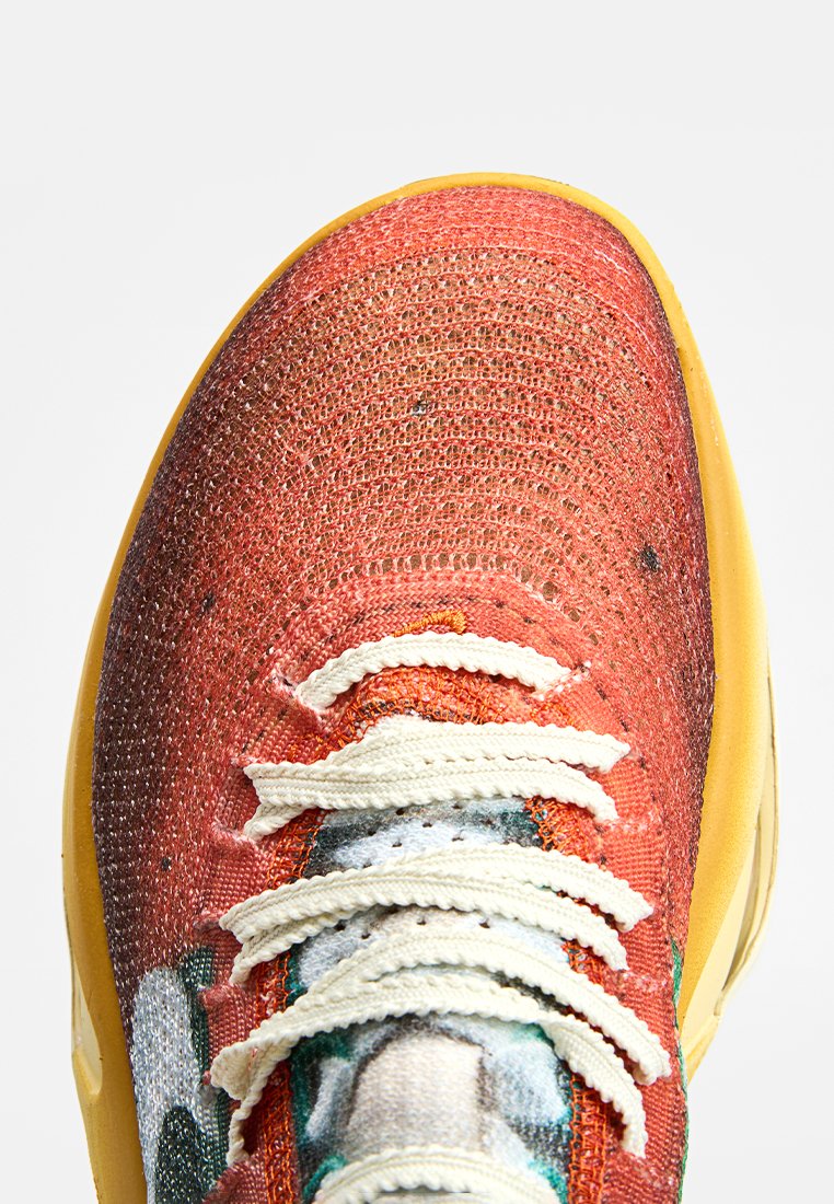 Baskets en mesh avec une tige texturée orange-rouge, des lacets crème et une semelle en caoutchouc jaune. Présente des motifs graphiques subtils sur le matériau.