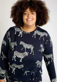 Camisa de manga larga azul marino con un patrón de cebra en blanco, hecha de un tejido suave, con un escote redondeado y un detalle anudado en la cintura.