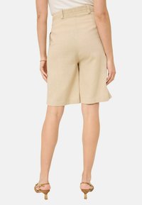 Beige skræddersyede Bermuda shorts med elastisk talje, med en glat tekstur og knælang skæring, båret med strappy brune hæle.
