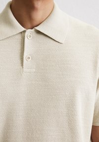 Beige textured polo shirt featuring a classic collar, two button placket, and a knitted fabric with a subtle pattern.