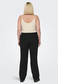 Svarta högmidjade byxor med en slät yta, kombinerat med en cremefärgad, ärmlös topp med tunna axelremmar.