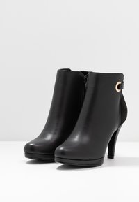 Mustat nilkkurit, jotka on valmistettu sileästä nahasta. Niissä on terävä kärki, kapea korkea korko, sivuvetoketju ja kultasävyinen koriste.