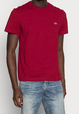 T-shirt en coton rouge à manches courtes, col rond et un petit logo vert. Assorti à un jean en denim bleu clair.