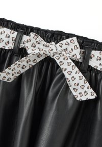 Gonna nera in finta pelle con texture arricciata, dotata di una cintura in tessuto bianco decorata con un motivo a cuore rosa e nero.