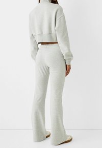 Felpa grigia corta con collo alto e maniche ampie abbinata a comodi pantaloni della tuta svasati nello stesso colore e con vita elastica.