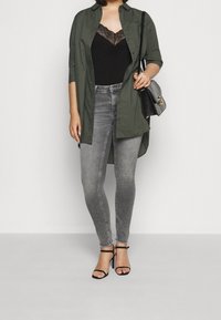 Black lace-trimmed camisole layered under an olive green button-up shirt, paired with light gray skinny jeans and black strappy heels.