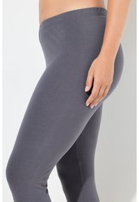 Leggings grises con textura suave, cintura elástica y diseño ajustado, vistos desde un ángulo lateral con características mínimas visibles.