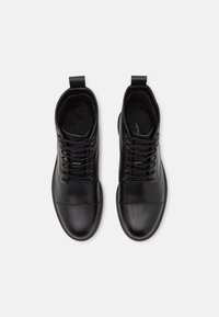 Paire de bottines noires en cuir à lacets avec bouts arrondis et languettes à l'arrière, vues de dessus sur un fond blanc.