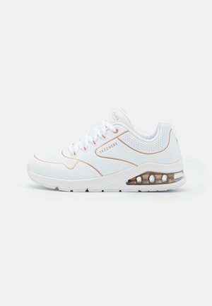 White Skechers sneaker with beige accents, perforated details, transparent air cushion sole, and white laces on a plain background.
