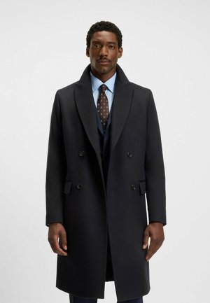 Navy wool blend double-breasted coat with wide lapels, button accents, and side pockets, worn over a blue shirt and tie.