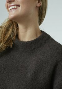 Brun uldtrøje med tekstureret finish, rund halsudskæring og ribbede ærmekanter. Stoffet virker blødt og let fnugget.