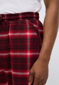 Κόκκινο και μαύρο καρό παντελόνι σπιτιού με ελαστική μέση και πλαϊνές τσέπες, φτιαγμένο από απαλό ύφασμα, με λευκές λ�επτομέρειες στο μοτίβο.