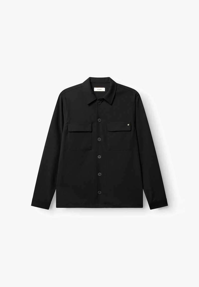Chemise noire à manches longues avec boutons-pression, deux poches à rabat sur la poitrine et un col classique, posée à plat sur un fond blanc.