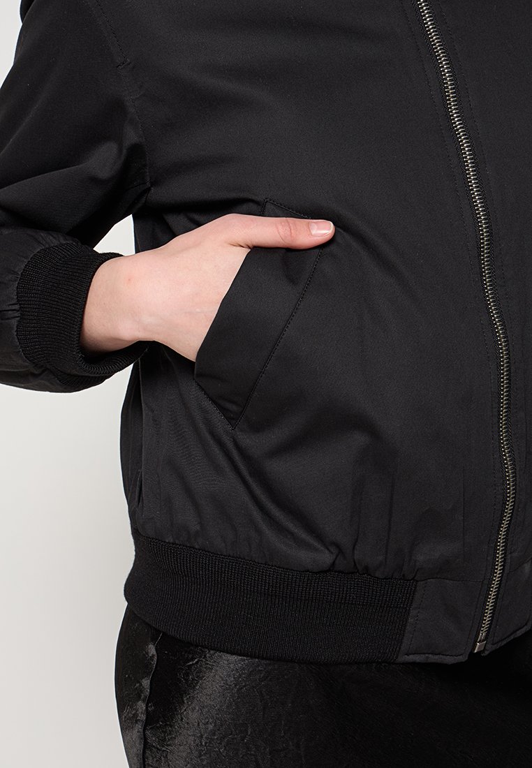 Czarna kurtka bomberka z zamkiem z przodu, ściągaczami na mankietach i u dołu oraz boczną kieszenią. Gładka tekstura i lekki materiał.