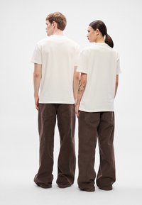 Kremowe t-shirty z krótkim rękawem w połączeniu z brązowymi spodniami o szerokich nogawkach, prezentujące prosty design i luźne dopasowanie, widoczne od tyłu.