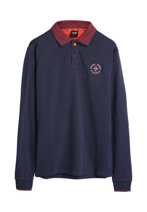 Marineblauw poloshirt met lange mouwen en een rode kraag, met een rond logo op de borst en contrasterende rode accenten op de manchetten.