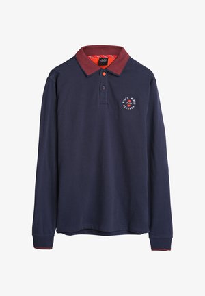 Marineblauw poloshirt met lange mouwen en een rode kraag, met een rond logo op de borst en contrasterende rode accenten op de manchetten.
