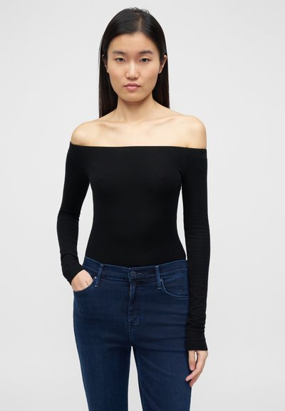 Must valge õlgadeta pikkade varrukatega bodi, keha järgnev lõige, pehme tekstuur, ühendatud tumeda pestud kõrge vöökohaga teksadega, nähtavate taskutega.