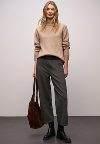 Beiger Pullover mit geripptem Kragen, graue strukturierte Hose, schwarze Stiefeletten und eine braune Wildleder-Umhängetasche. Einfaches, modernes Outfit.