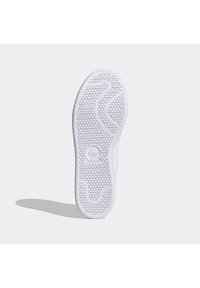 Vit sneakersula med ett strukturerat hexagonmönster och släta kanter, med en präglad logotyp i mitten. Platt och böjd design.