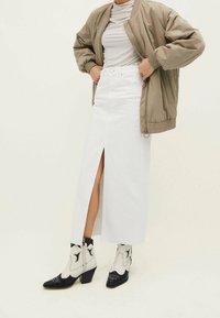 Witte denimrok met een voorventilatie, gecombineerd met een lichtgrijze top en een beige bomberjack; voorzien van zwart-witte cowboylaarzen.