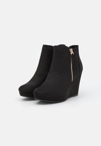 Černé klínové kotníkové boty vyrobené z měkké nubukové kůže. Mají boční zip a kulatý tvar špičky. Hladký povrch s elegantním siluetou.