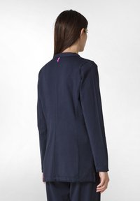 Mörkblå långärmad jacka med en figursydd passform, med en rund krage och en rosa detalj vid nacklinjen bak. Tillverkad av en slät tyg.