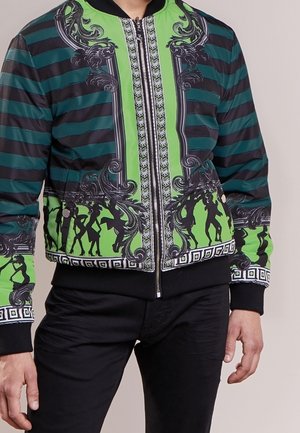 Kurtka na zamek z zielono-czarnymi poziomymi pasami, misternymi czarnymi wzorami barokowymi i sylwetkami tańczących postaci wzdłuż brzegu.