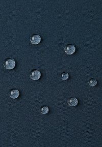 Krople wody na ciemnoniebieskiej teksturowanej tkaninie, ukazujące gładką powierzchnię z delikatnymi refleksami i różnymi rozmiarami kropli.